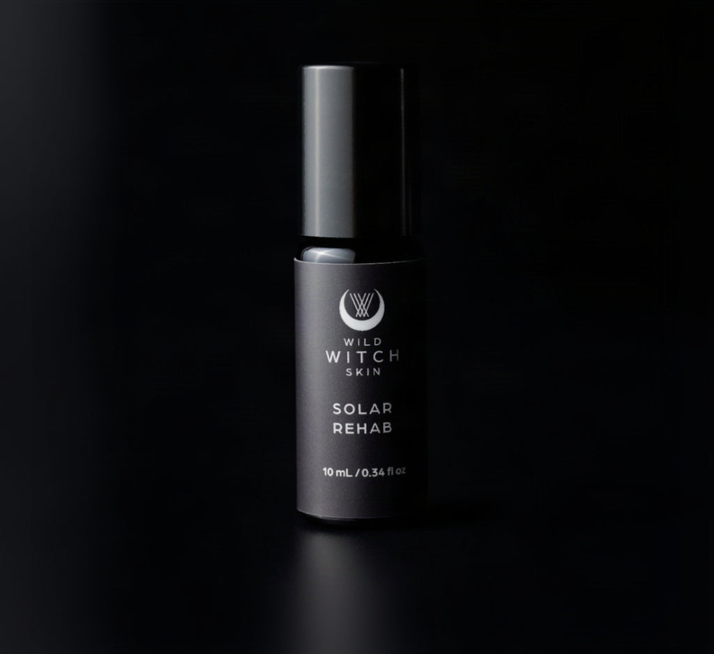 A single cylindrical cosmetic bottle labeled 'Wild Witch Skin Solar Rehab' in matte black, photographed against a solid black background.
