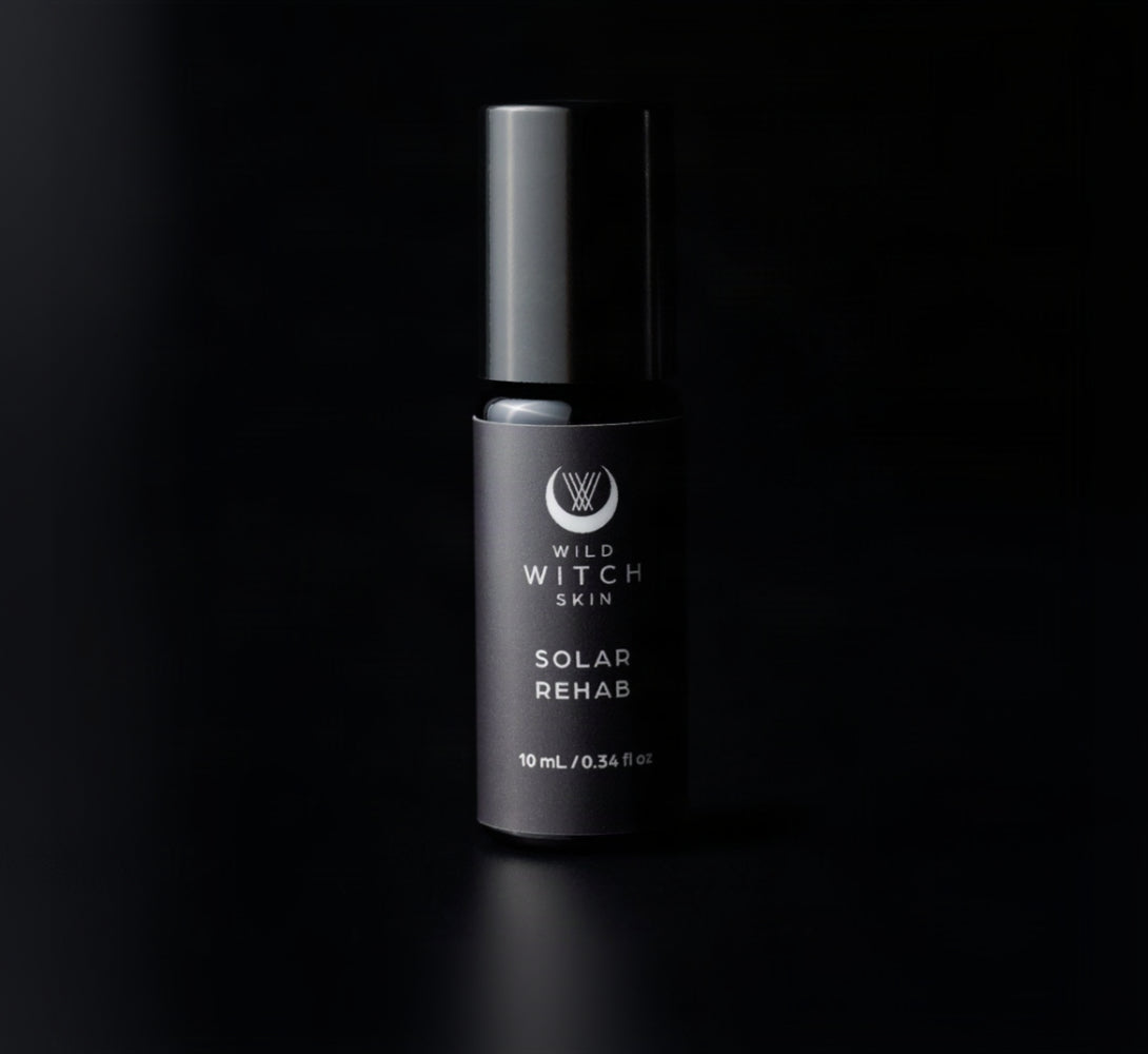 A single cylindrical cosmetic bottle labeled 'Wild Witch Skin Solar Rehab' in matte black, photographed against a solid black background.